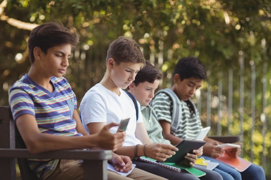 School kids using mobile phone and digital tablet on bench