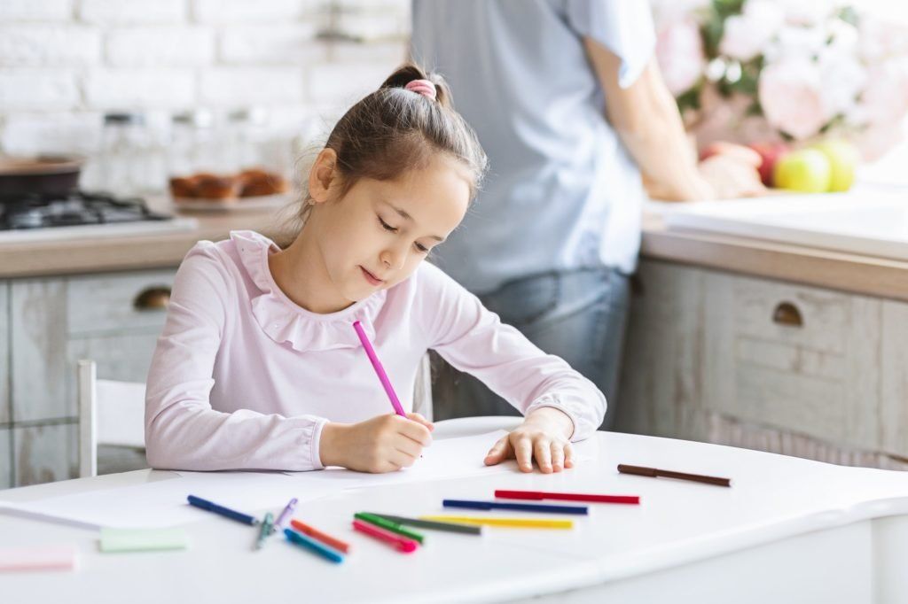 Pretty little girl busy with drawing at kitchen table