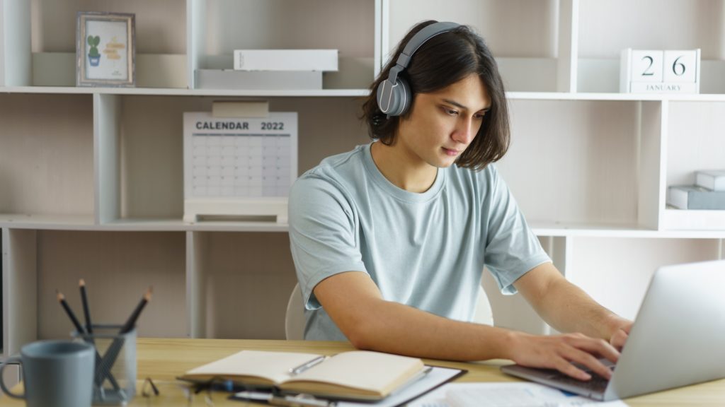 Distance education concept, Teen boy wear headphone to lesson class online and type chat in skype.