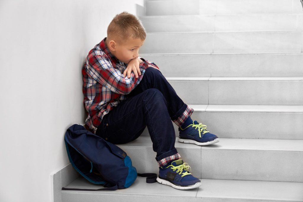 Little school boy sitting alone on stairs on school