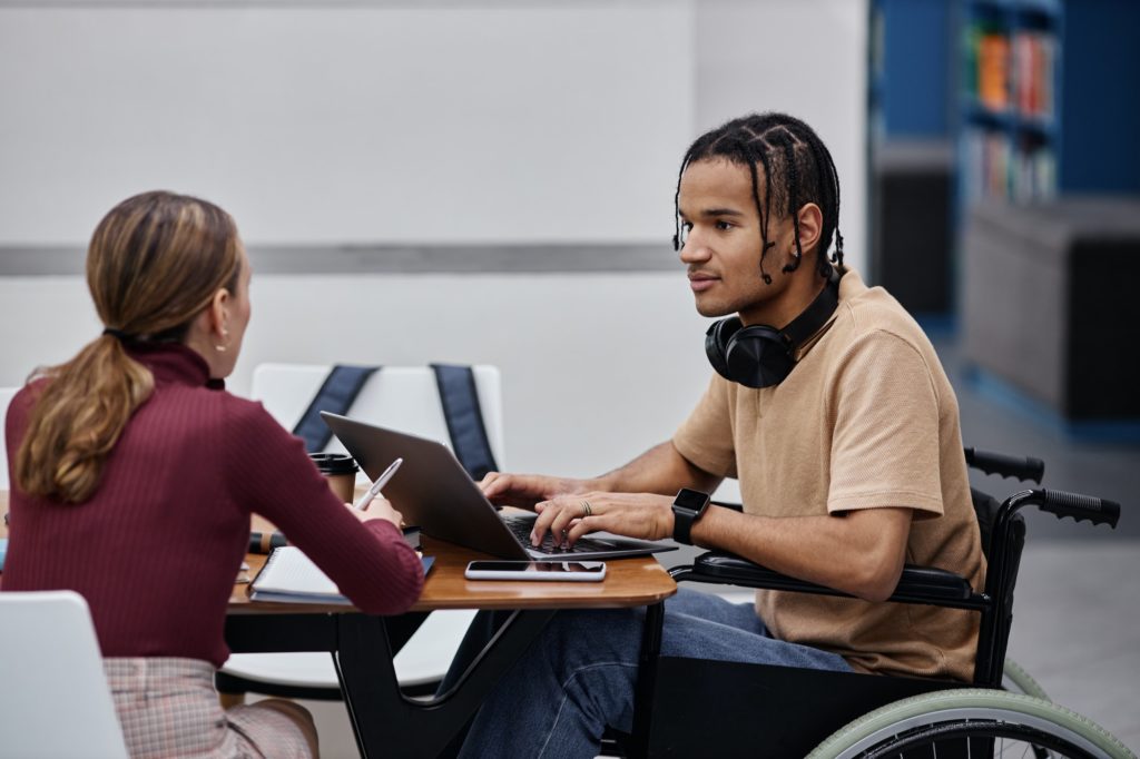 Young black boy with disability studying in college library with friend